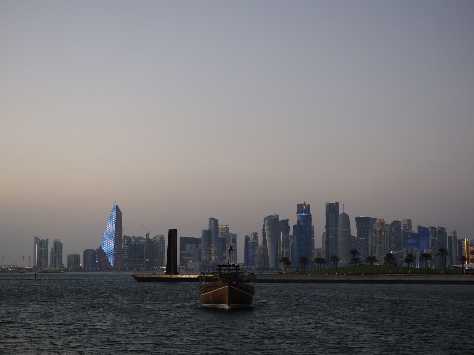 Doha waterfront skyline at dusk with a traditional dhow boat in the foreground