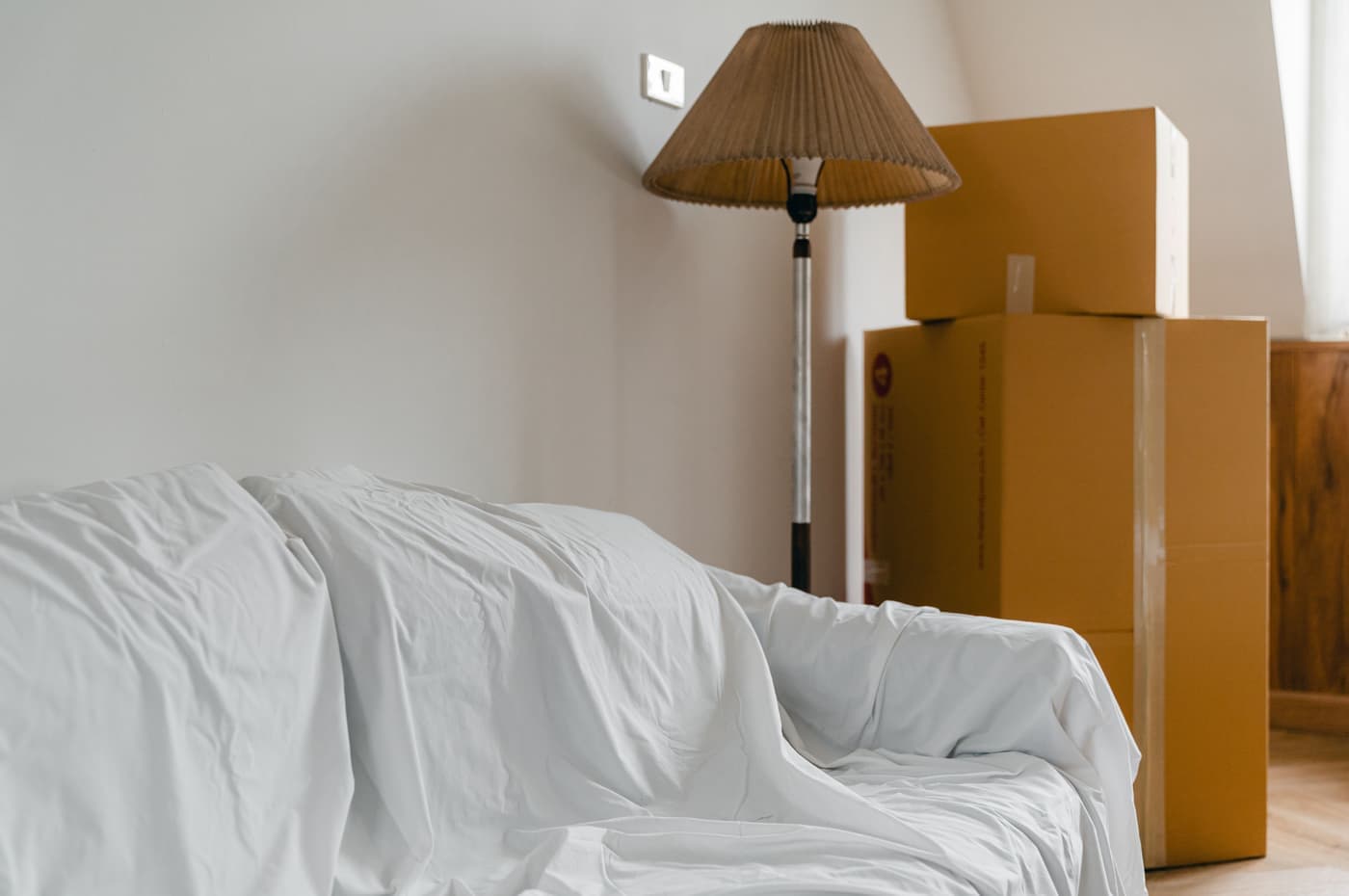 A sofa under a dust sheet beside packed cardboard boxes in an emptied room