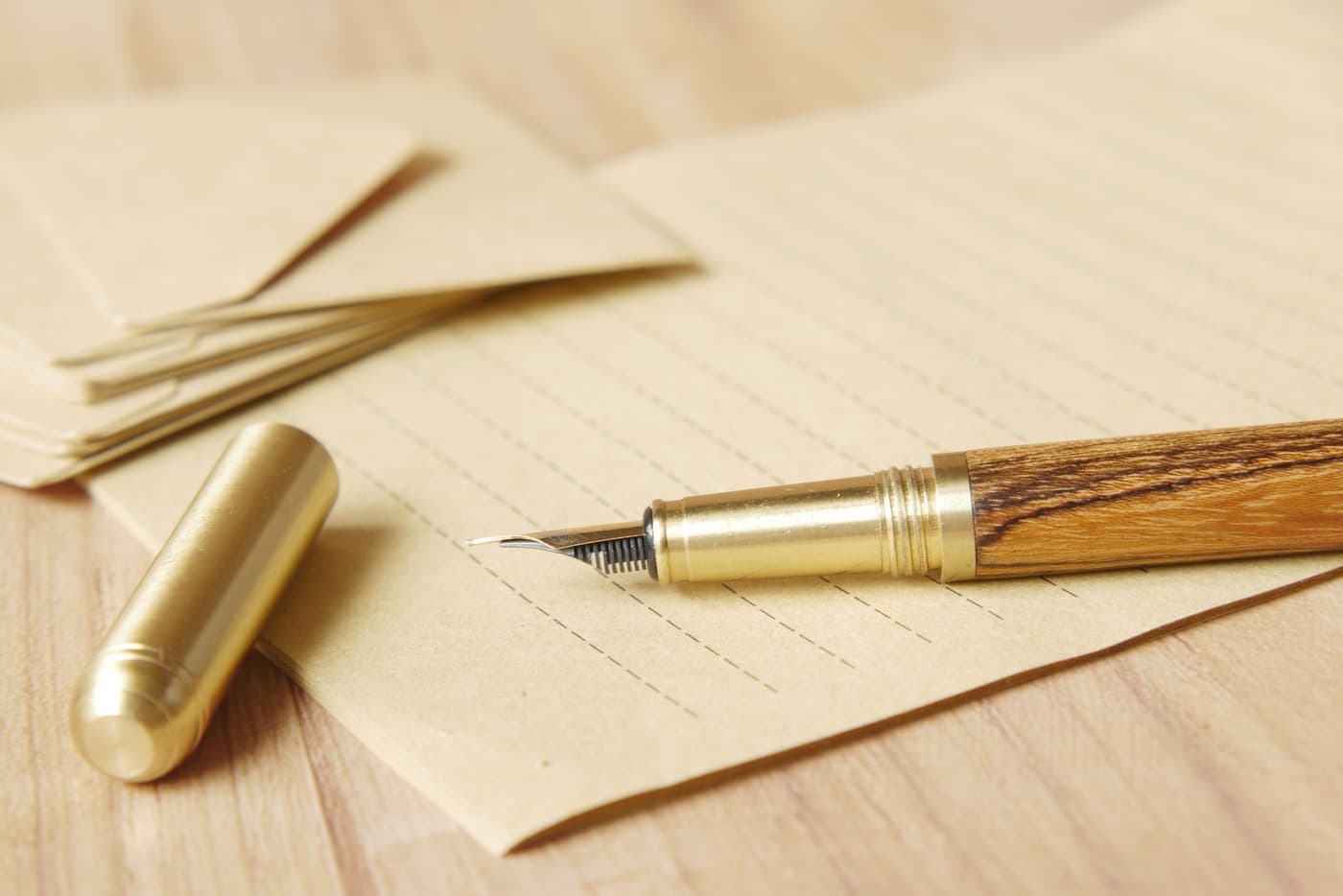 Gold fountain pen resting on lined writing paper and a brown envelope