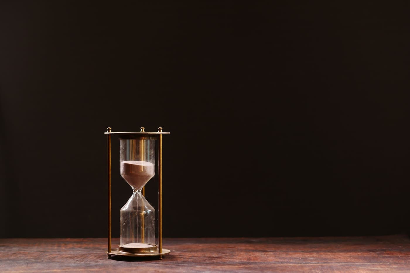 Hourglass with sand trickling down against a dark background