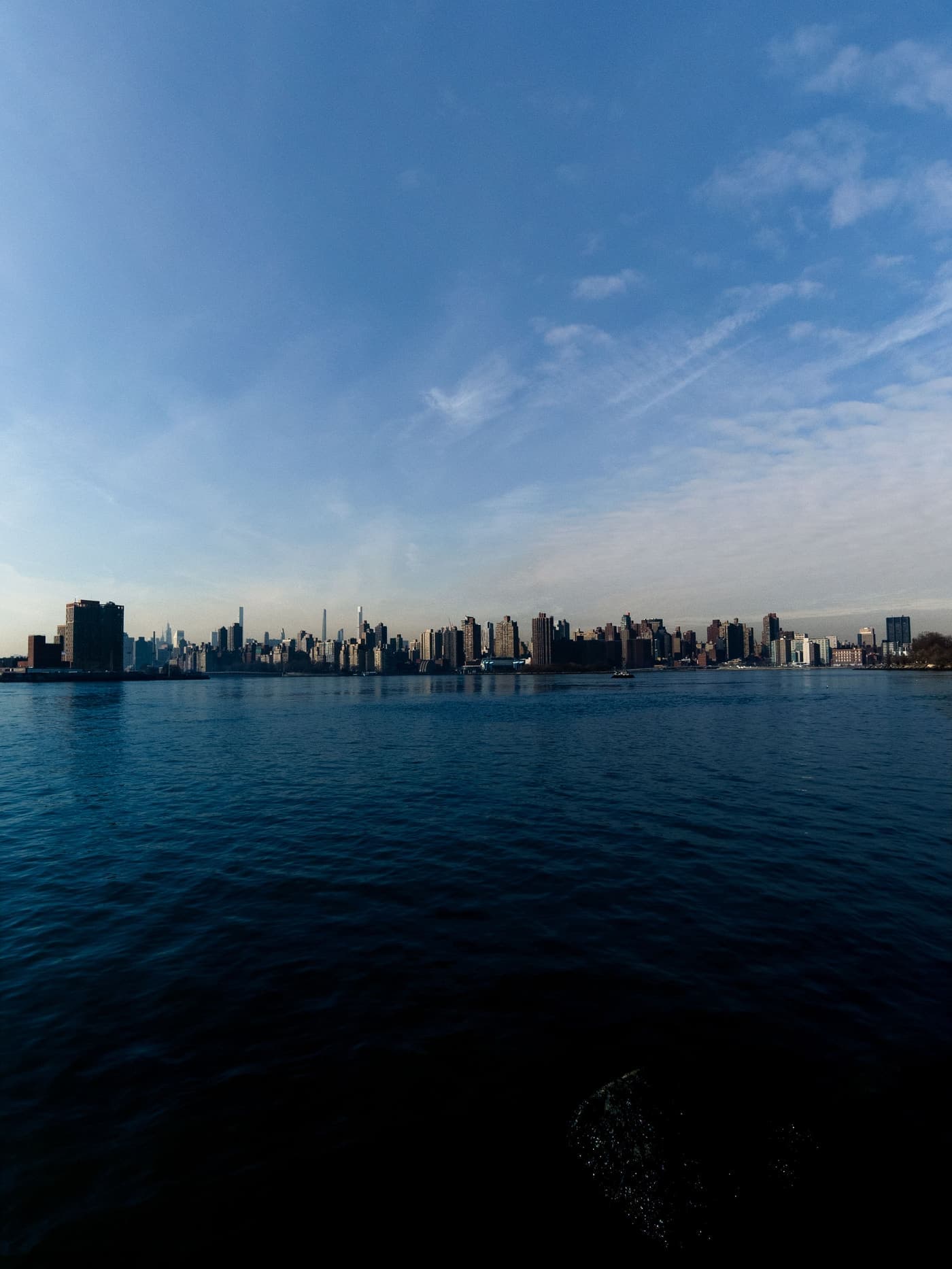 Manhattan skyline seen across calm water under a blue sky