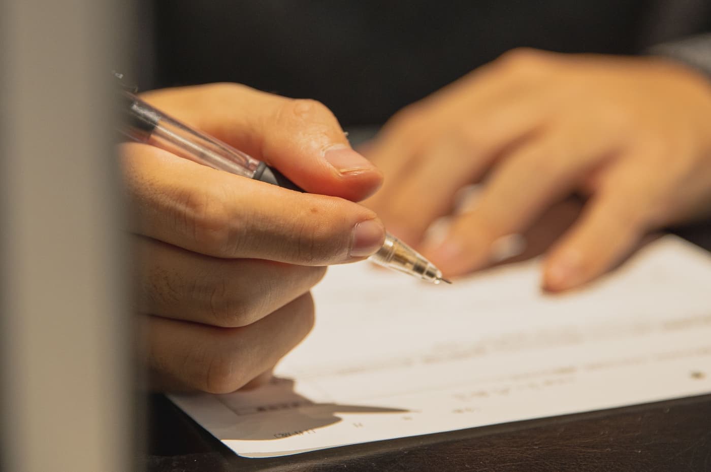 A person filling in a printed form with a pen at a table
