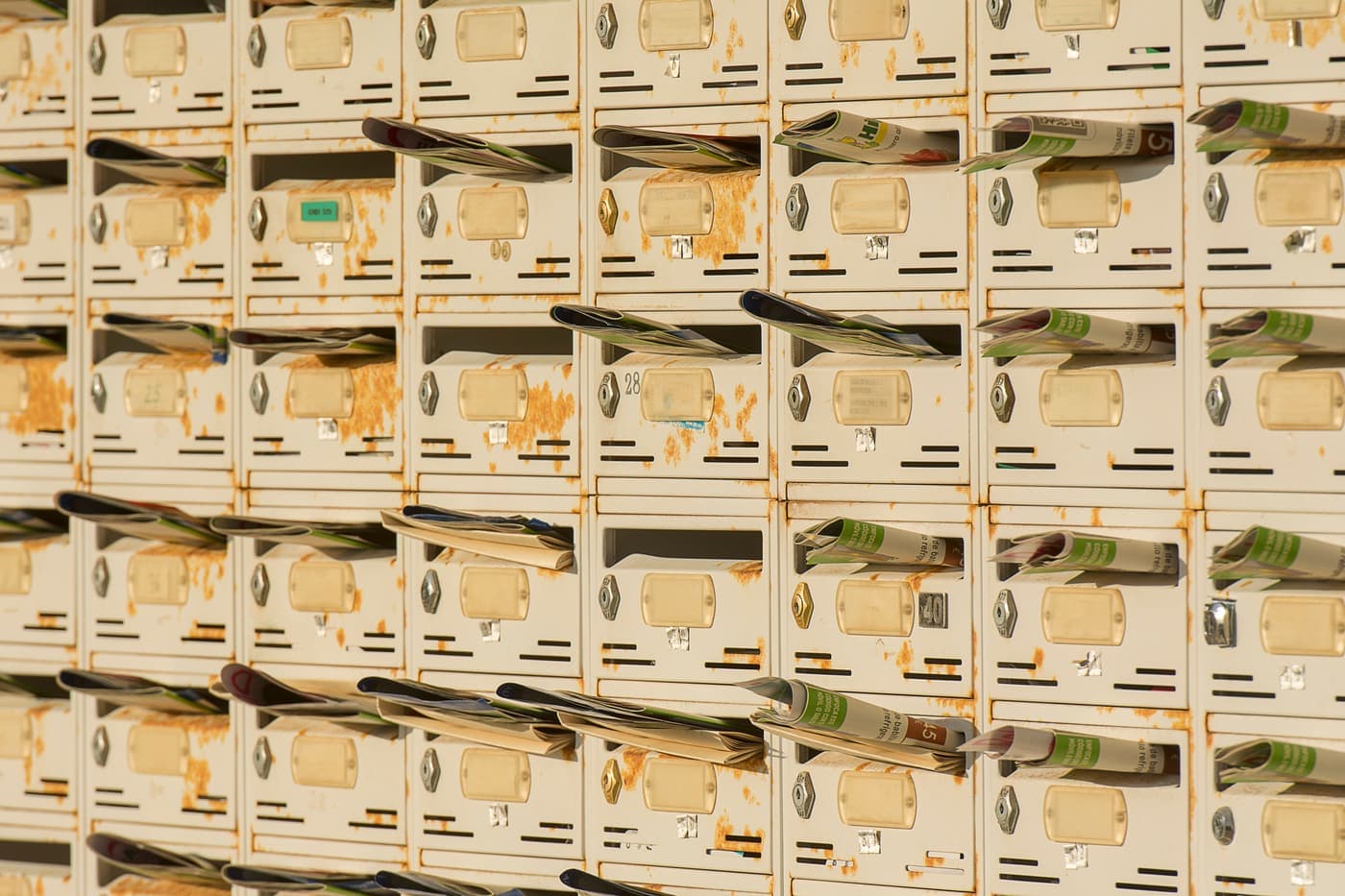Row of metal pigeonhole mailboxes filled with folded papers