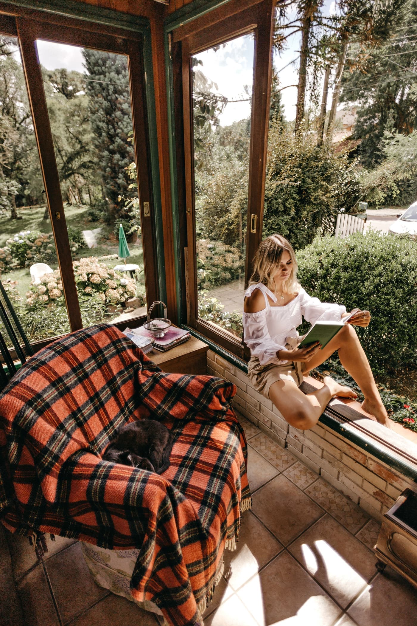 Woman reading a book on a window sill overlooking a garden