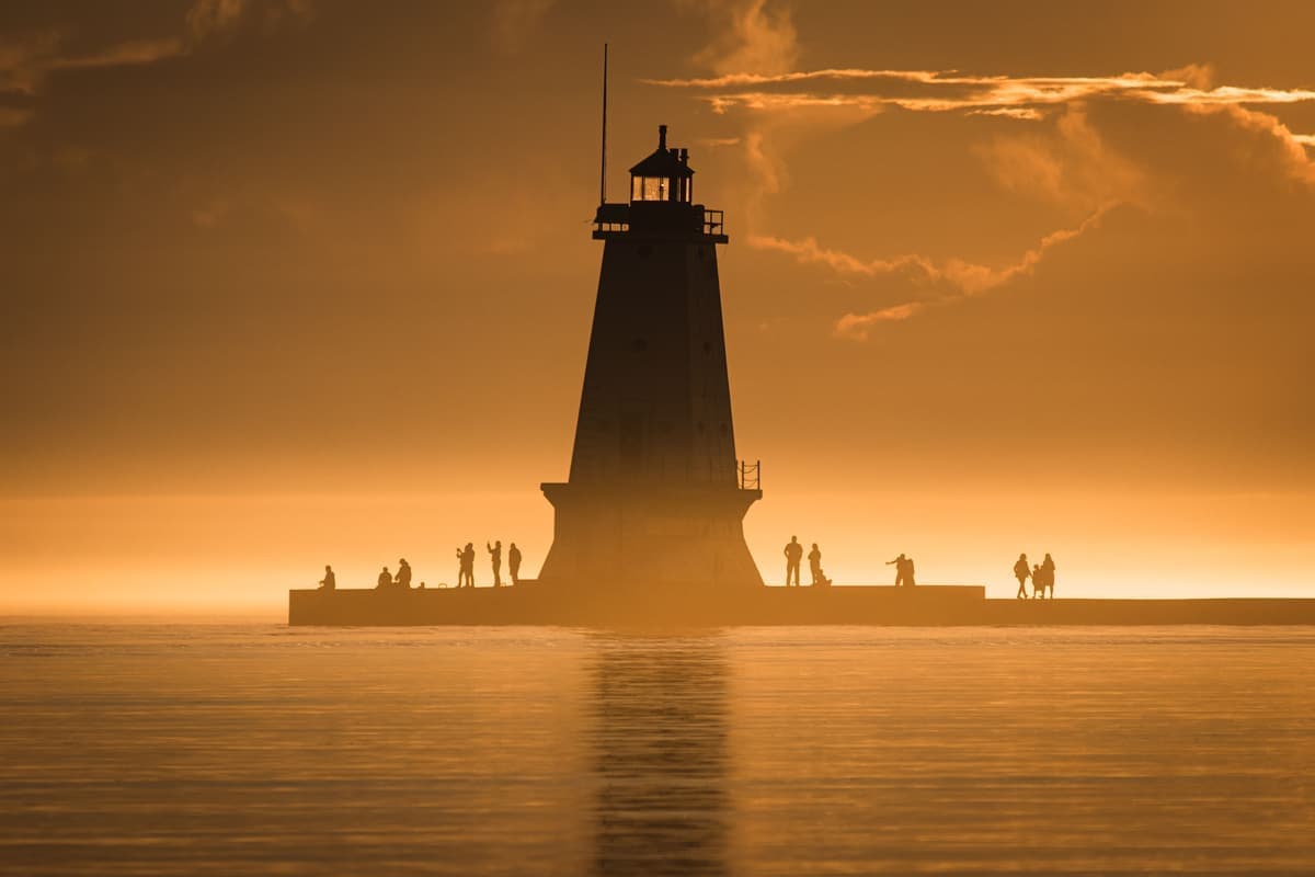 A lighthouse standing on a headland with its light visible against the evening sky