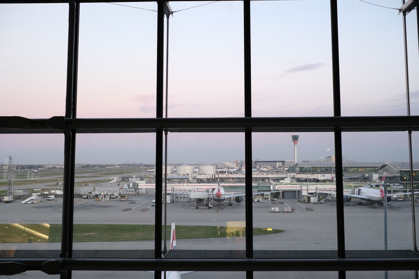 Aircraft on the Heathrow tarmac seen through a terminal window at twilight
