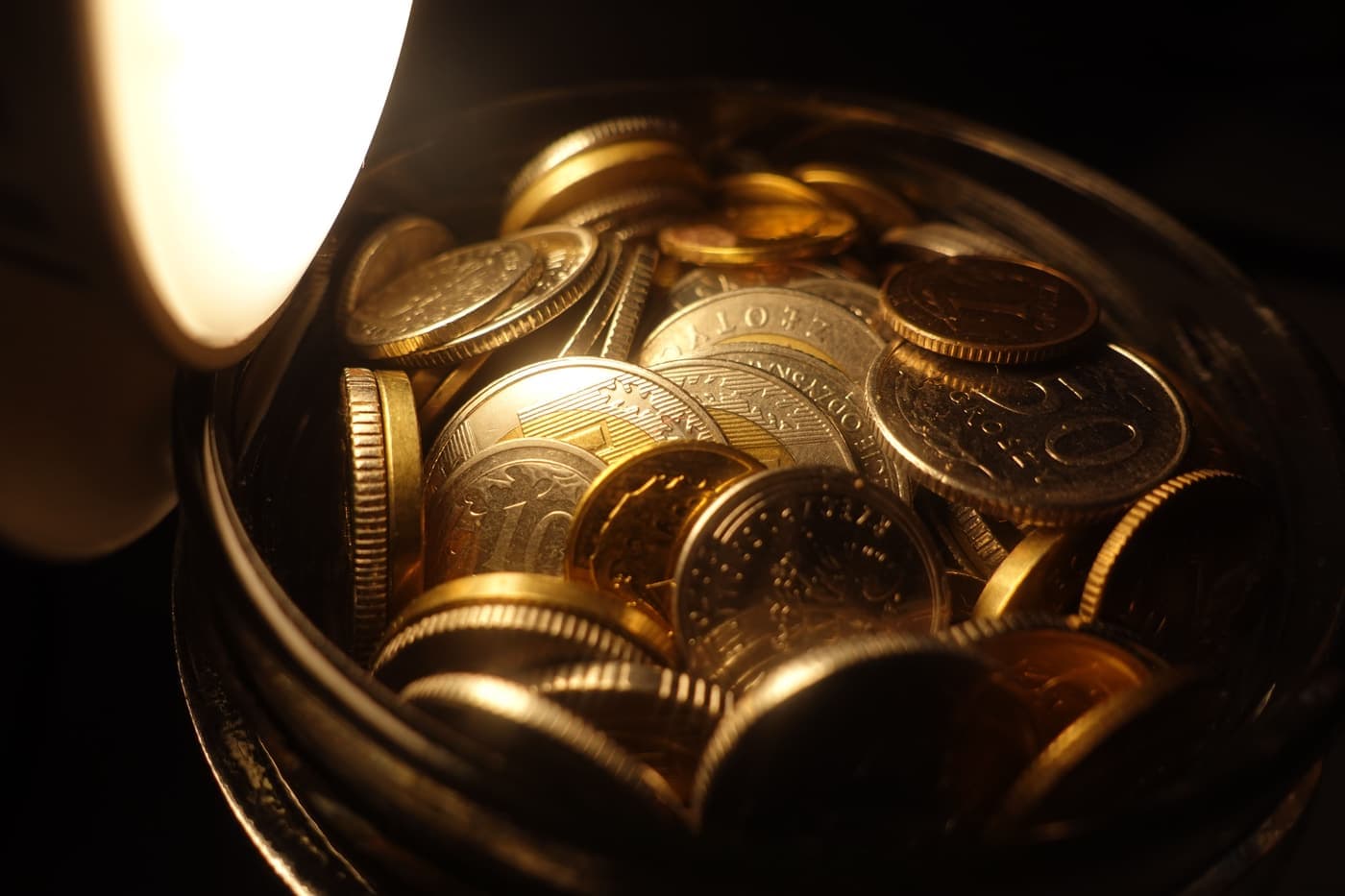 Assorted coins in a glass jar under warm light