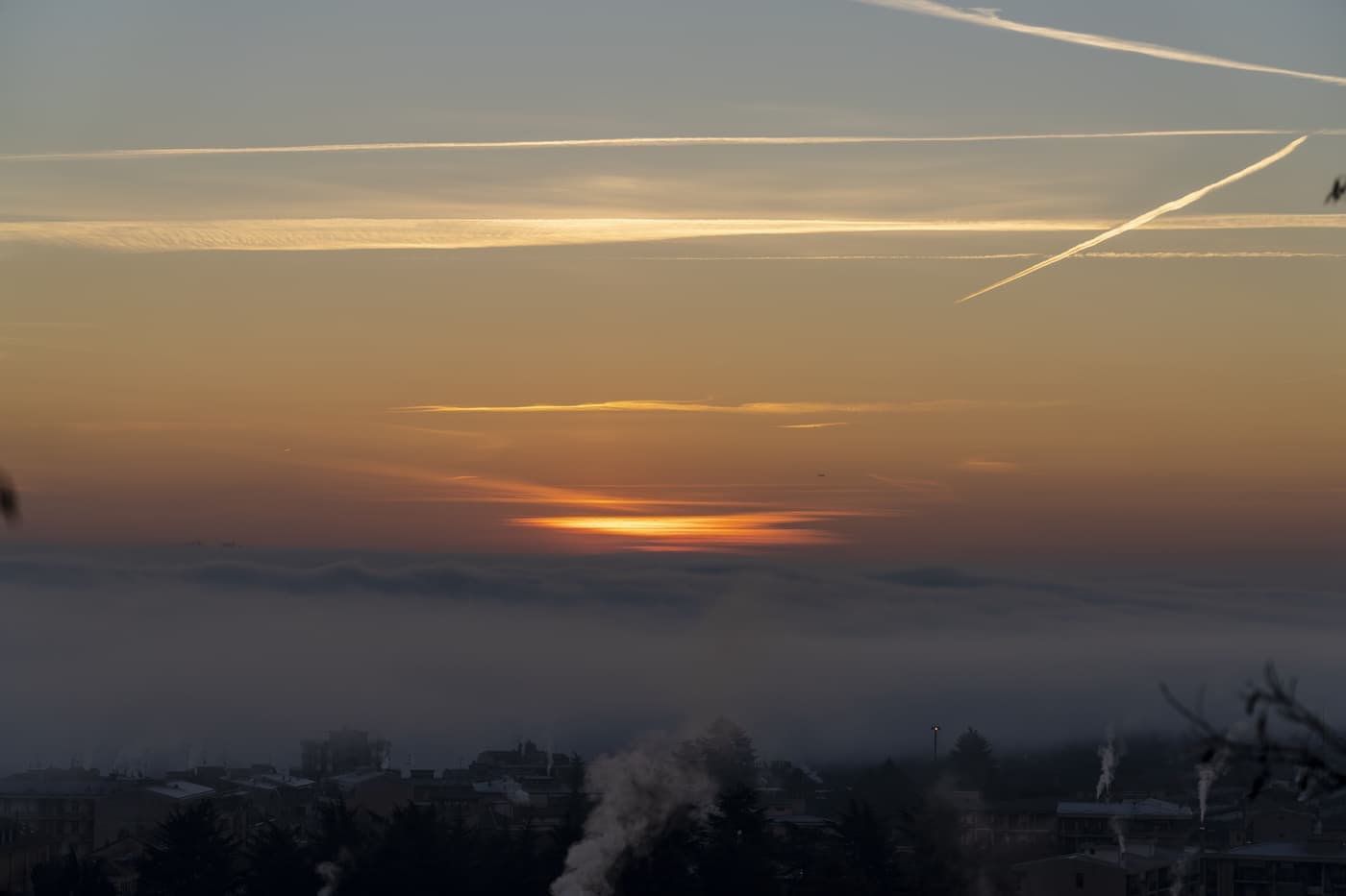 Aircraft contrails above a mist-covered city at sunrise