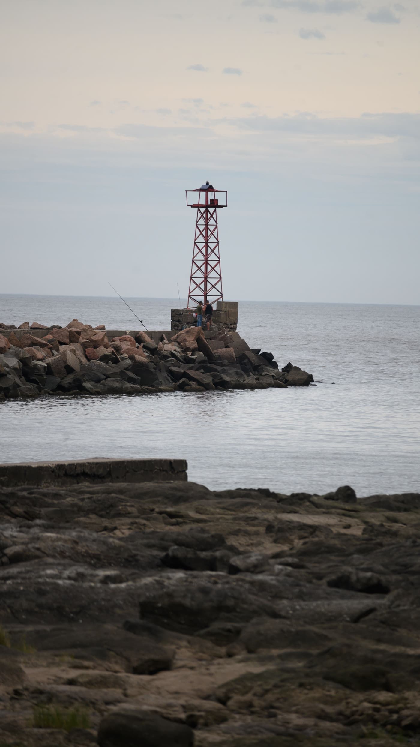 Steel lighthouse on a breakwater beside a calm sea under soft cloud