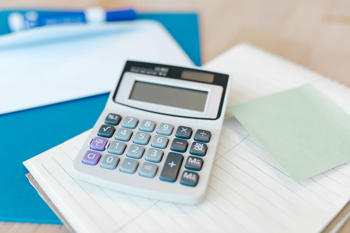 A calculator resting on a pad of lined paper beside a folder.