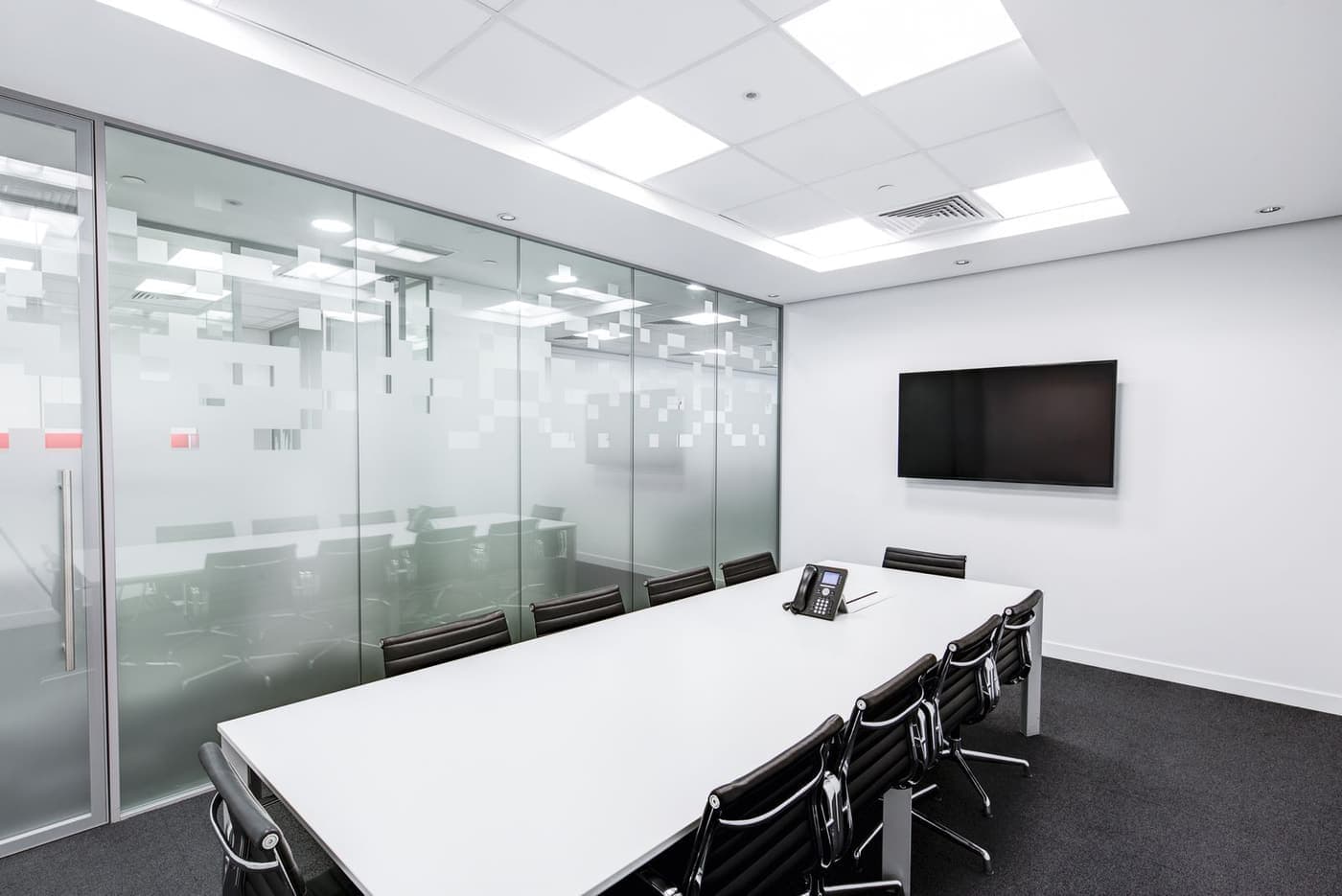 An empty boardroom table lit by daylight through glass walls.