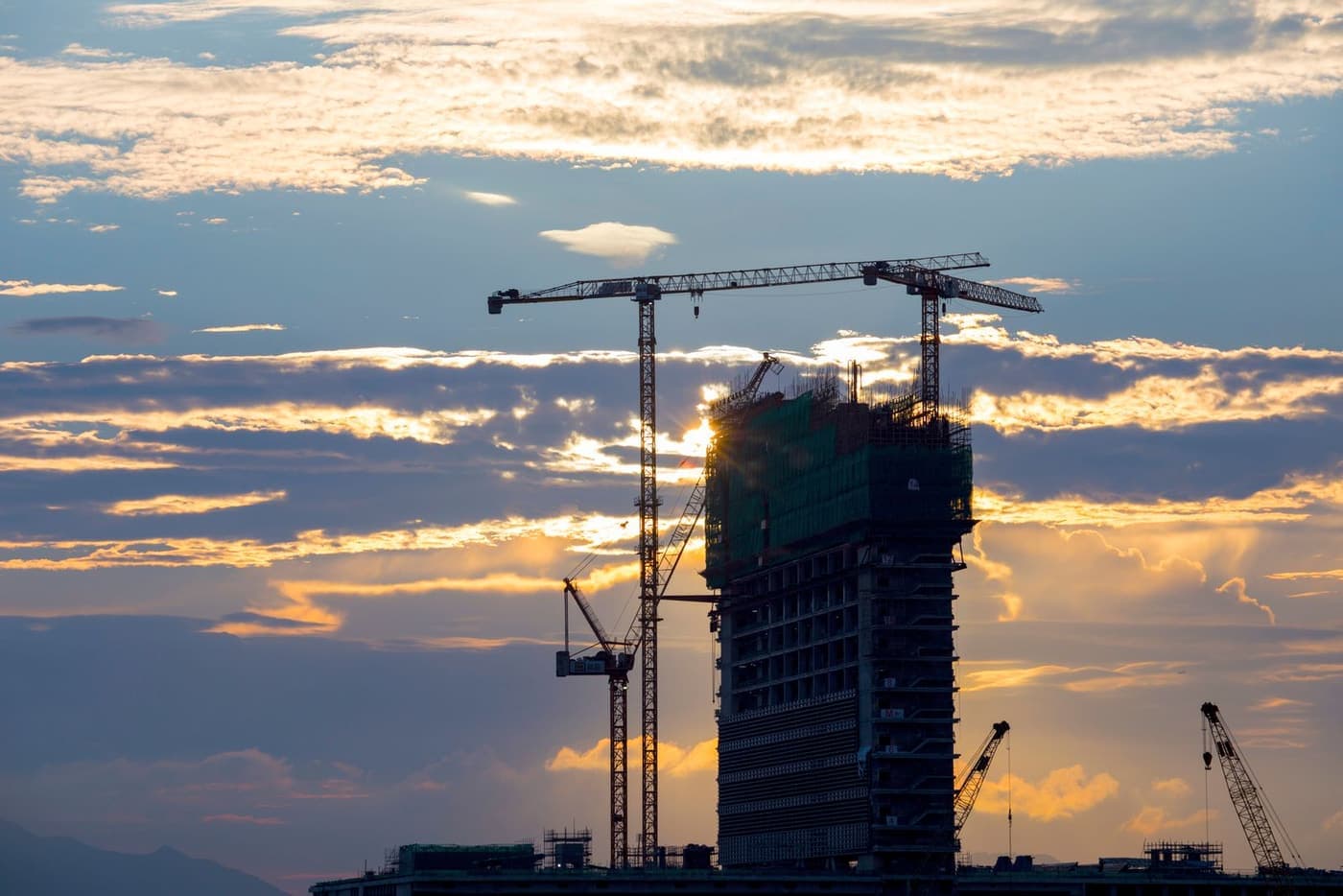 A building under construction with a tower crane at dusk.