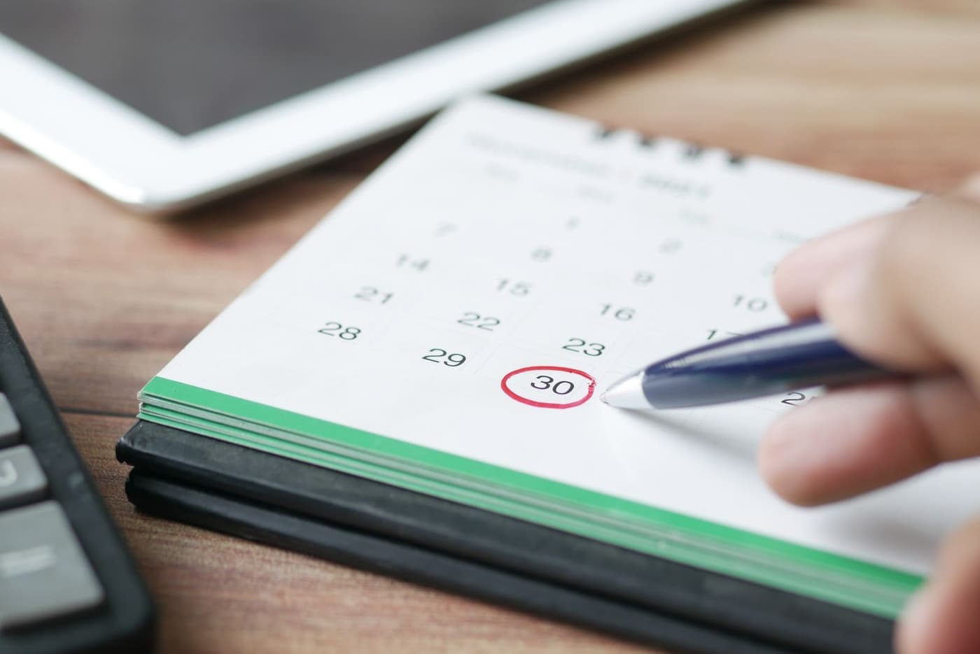 A date being marked on a desk calendar with a pen.