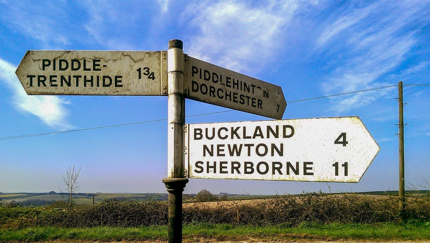Vintage metal signpost pointing towards English villages under a clear sky